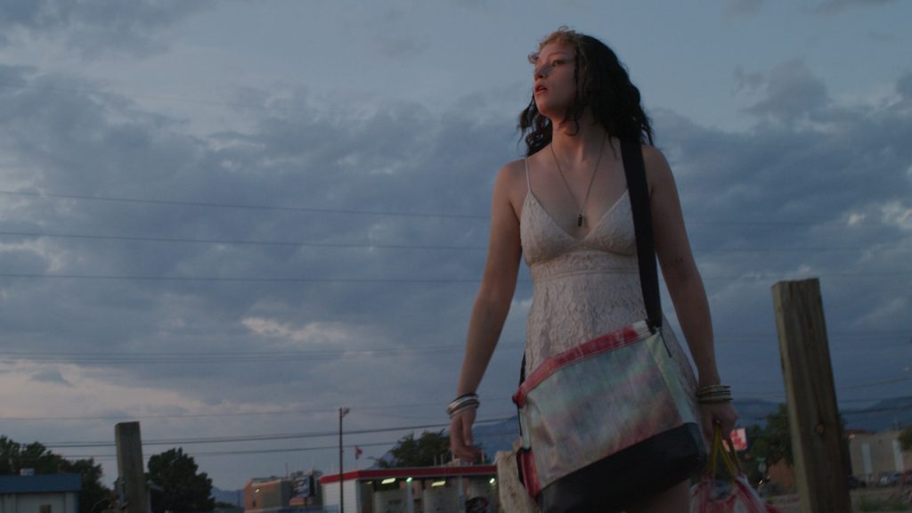 a frame from Drifteen depicting a young woman walking with a cloudy sky behind