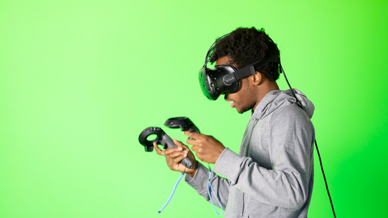a student plays with a VR headset in front of a green screen