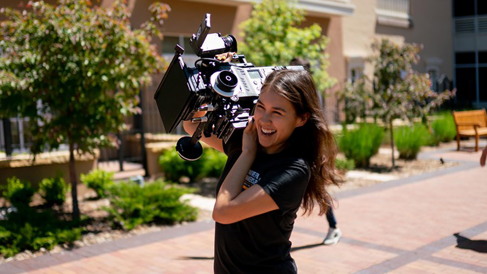 A film student smiles and holds a camera over her shoulder