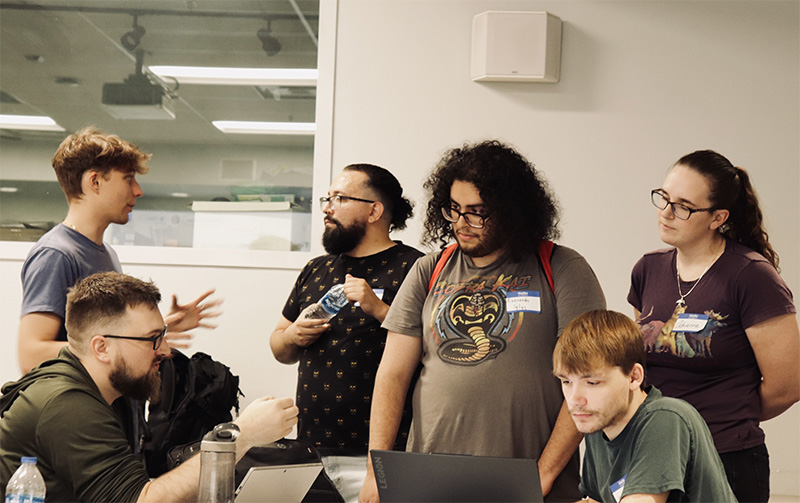 a group of students conversing around a monitor